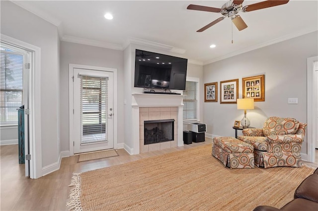 living room with ornamental molding, light wood-type flooring, a tiled fireplace, and ceiling fan