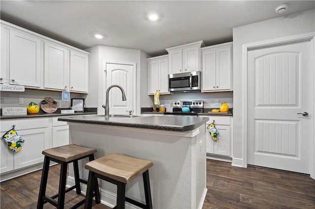 kitchen featuring appliances with stainless steel finishes, sink, white cabinets, a kitchen bar, and a kitchen island with sink