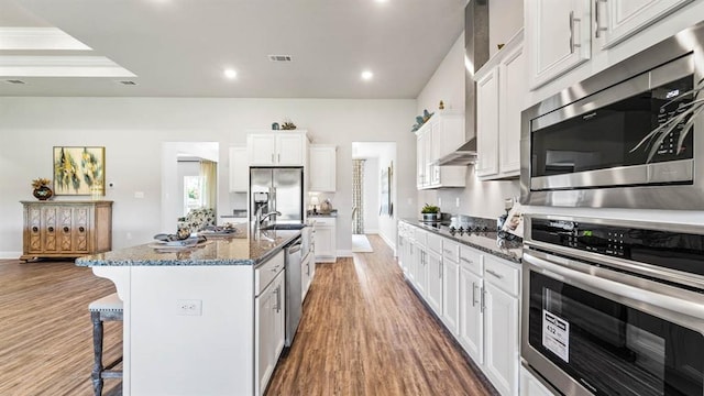 2260 Nadine Ln, Mobile, AL 36695 - kitchen featuring appliances with stainless steel finishes, a kitchen breakfast bar, wood finished floors, dark stone countertops, and a kitchen island with sink