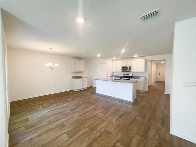 kitchen featuring appliances with stainless steel finishes, dark wood-type flooring, pendant lighting, white cabinetry, and an island with sink