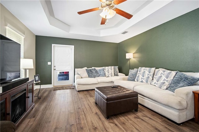 living room with hardwood / wood-style flooring, a raised ceiling, and ceiling fan