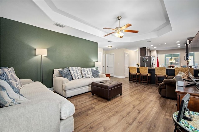 living room featuring ceiling fan, a raised ceiling, and light wood-type flooring