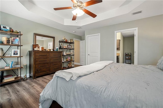 bedroom with a tray ceiling, ensuite bath, ceiling fan, and wood-type flooring