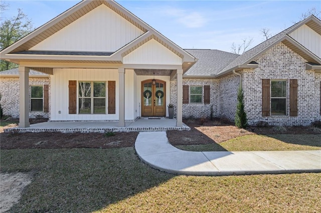 view of front facade with brick siding, roof with shingles, covered porch, french doors, and a front yard