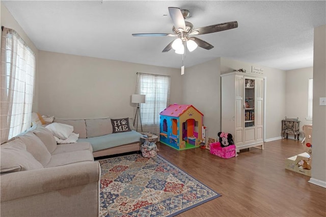 living area featuring ceiling fan, baseboards, and wood finished floors