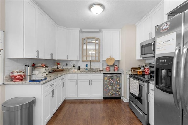 kitchen with dark wood finished floors, appliances with stainless steel finishes, light stone counters, white cabinetry, and a sink