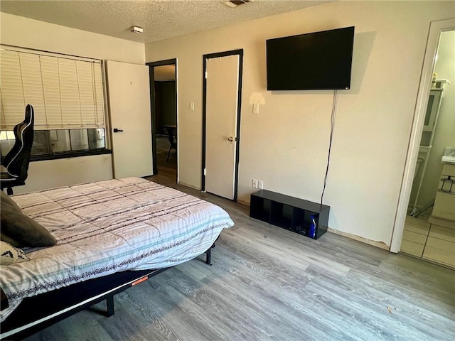 bedroom with wood-type flooring, connected bathroom, and a textured ceiling