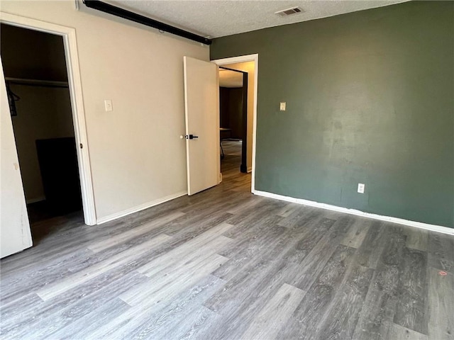 unfurnished bedroom with hardwood / wood-style flooring, a walk in closet, and a textured ceiling