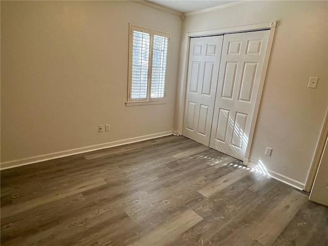 unfurnished bedroom with dark hardwood / wood-style flooring, crown molding, and a closet