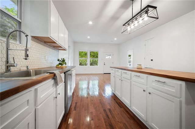 kitchen with dark wood finished floors, wooden counters, decorative backsplash, stainless steel dishwasher, and a sink