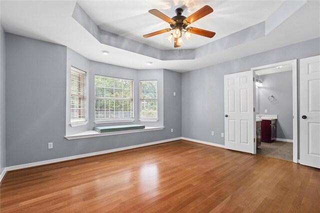 405 Baker Rd, Satsuma, AL 36572 - unfurnished bedroom featuring wood finished floors, baseboards, a tray ceiling, ensuite bathroom, and a ceiling fan