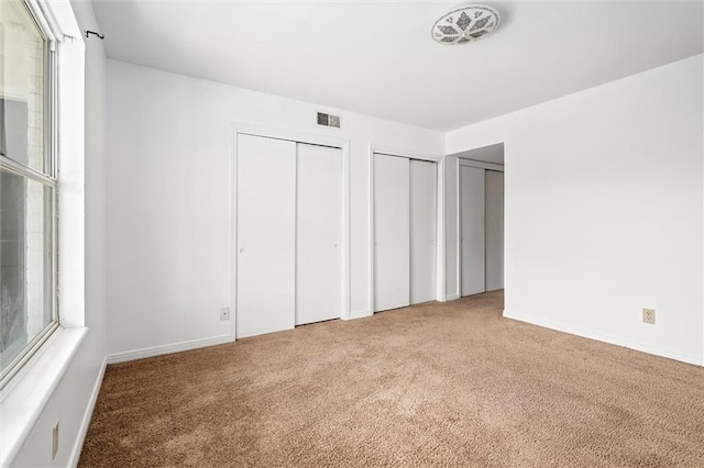 unfurnished bedroom with carpet floors and two closets