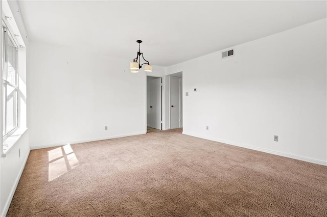 carpeted spare room featuring a chandelier