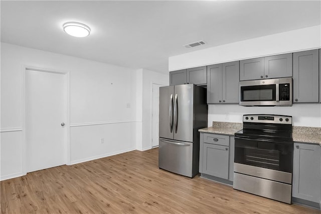 kitchen featuring gray cabinets, light stone countertops, stainless steel appliances, light wood-style floors, and visible vents