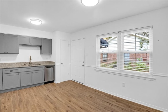 kitchen featuring stainless steel dishwasher, gray cabinetry, light wood finished floors, and a sink