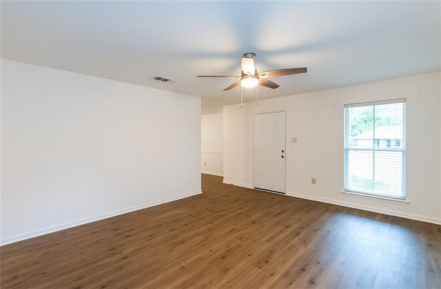 unfurnished room with visible vents, a ceiling fan, dark wood finished floors, and baseboards