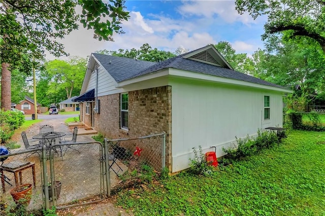 view of property exterior with a gate, a lawn, brick siding, roof with shingles, and fence