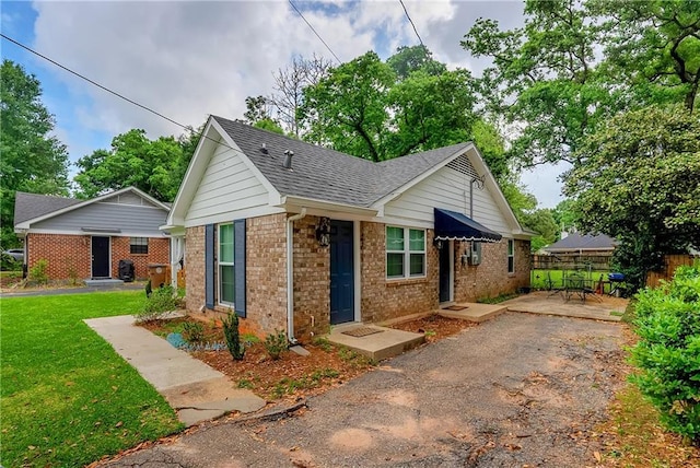 bungalow featuring a front lawn, roof with shingles, fence, and brick siding