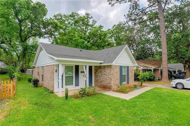 single story home featuring a front lawn, fence, roof with shingles, and brick siding