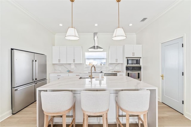 kitchen featuring stainless steel appliances, wall chimney range hood, a center island with sink, and white cabinets