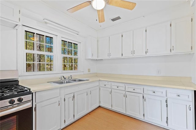 kitchen featuring stainless steel gas stove, crown molding, white cabinetry, and sink