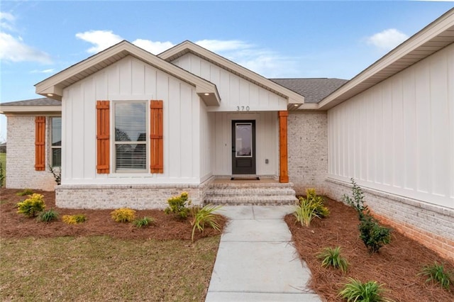 doorway to property with brick siding, board and batten siding, and a shingled roof