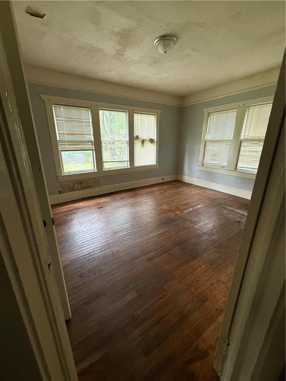 unfurnished room with baseboards, a textured ceiling, and dark wood-type flooring