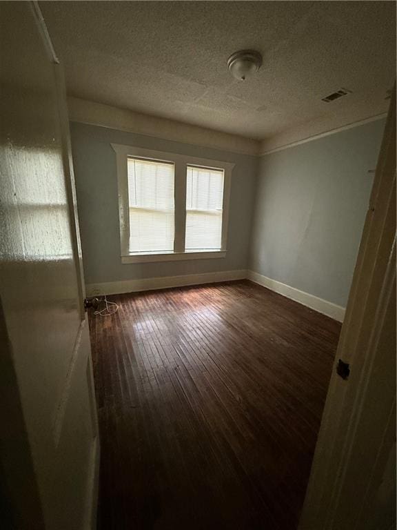 empty room with a textured ceiling, baseboards, dark wood-style flooring, and visible vents