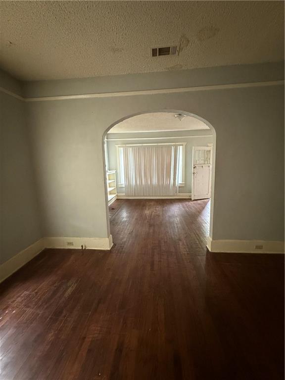 unfurnished room featuring arched walkways, dark wood finished floors, and baseboards
