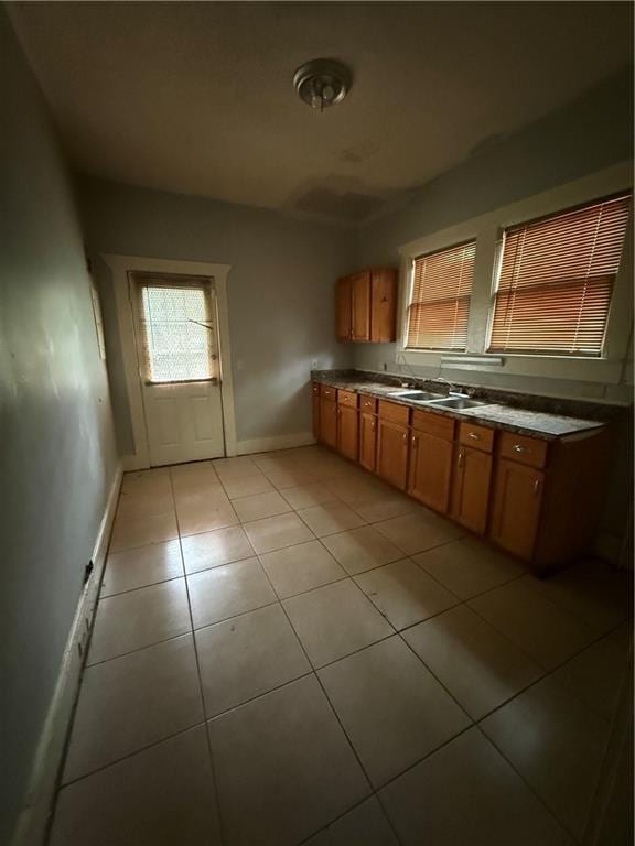 kitchen featuring brown cabinetry, baseboards, a sink, and light tile patterned floors