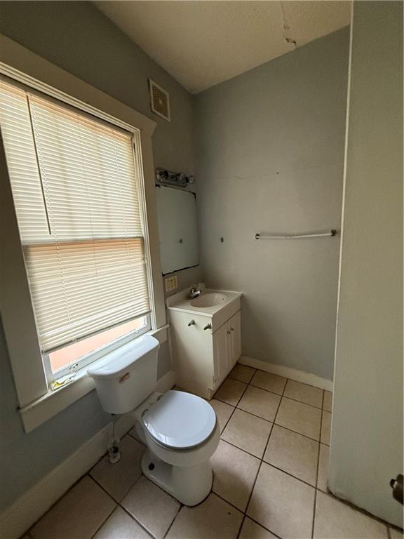 half bath with tile patterned floors, visible vents, toilet, vanity, and baseboards