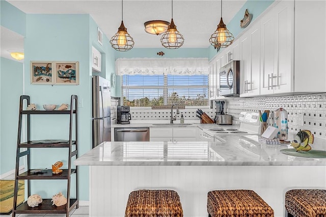 kitchen featuring decorative backsplash, white cabinets, appliances with stainless steel finishes, a peninsula, and a sink