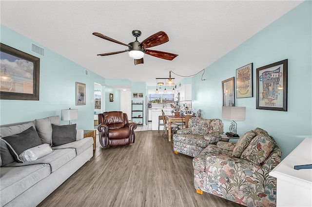 living room featuring ceiling fan, a textured ceiling, wood finished floors, and visible vents