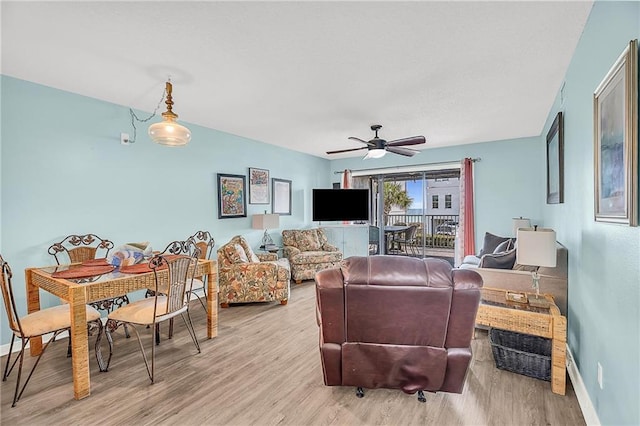 living area featuring baseboards, ceiling fan, and light wood finished floors