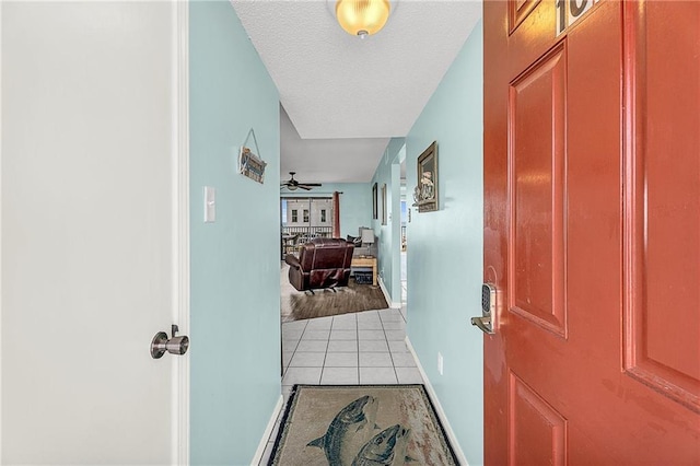 hall with a textured ceiling, baseboards, and tile patterned floors