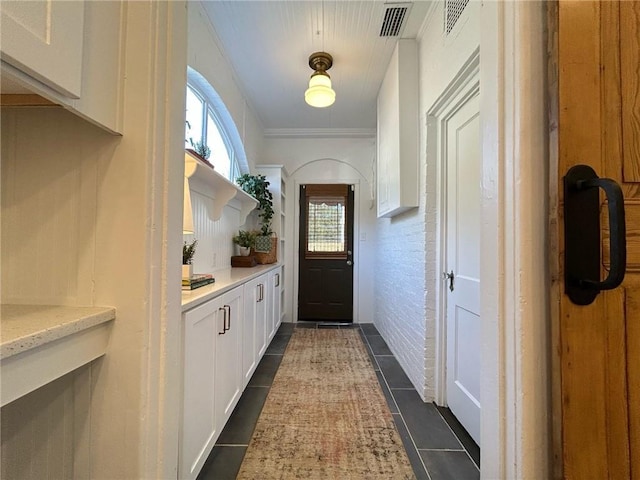 doorway featuring dark tile patterned flooring, crown molding, and brick wall