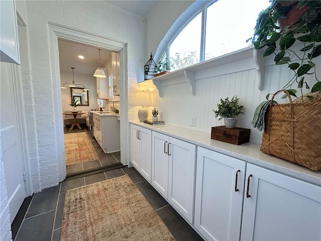 interior space with sink, white cabinetry, light stone counters, dark tile patterned flooring, and pendant lighting