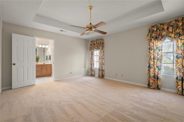 unfurnished bedroom featuring light carpet, ensuite bath, a raised ceiling, and ceiling fan