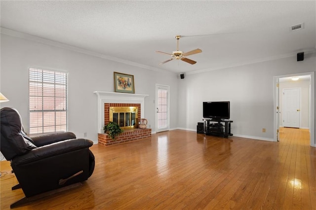 living room featuring a brick fireplace, light hardwood / wood-style flooring, ornamental molding, and ceiling fan