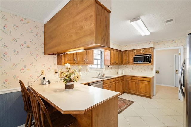 kitchen with sink, a breakfast bar area, appliances with stainless steel finishes, a textured ceiling, and kitchen peninsula