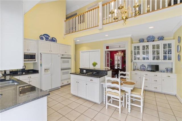 kitchen featuring white appliances, a towering ceiling, a chandelier, light tile patterned flooring, and a sink