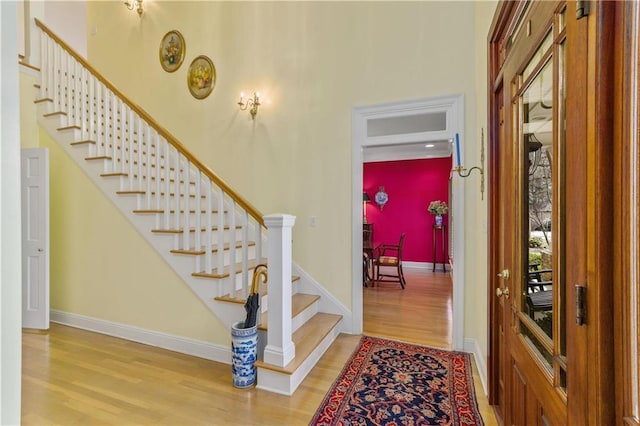 foyer entrance featuring wood finished floors, stairs, baseboards, and a high ceiling