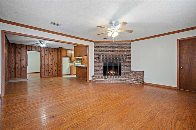 unfurnished living room featuring ornamental molding, a brick fireplace, a ceiling fan, and light wood-style floors