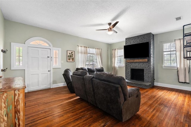 living room with dark wood-style floors, visible vents, plenty of natural light, and a fireplace