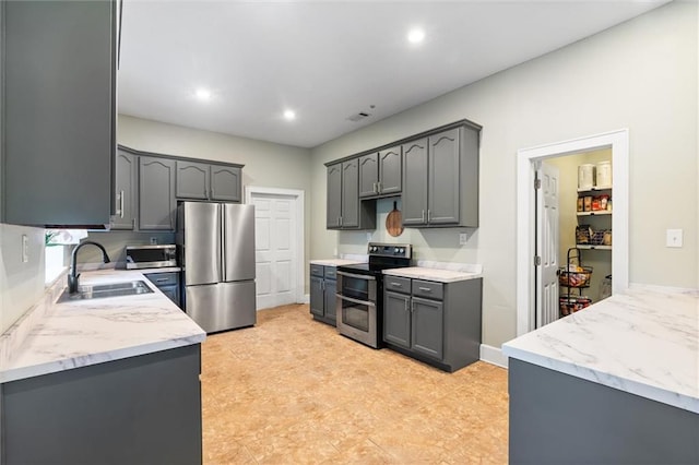 kitchen with gray cabinets, appliances with stainless steel finishes, light stone countertops, and a sink