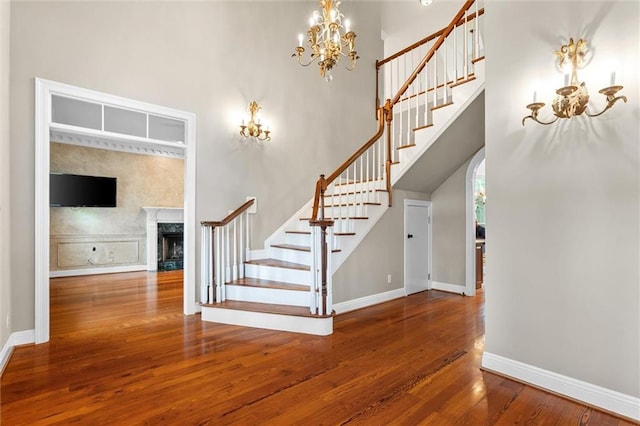 stairs featuring a notable chandelier, a towering ceiling, hardwood / wood-style floors, and a fireplace