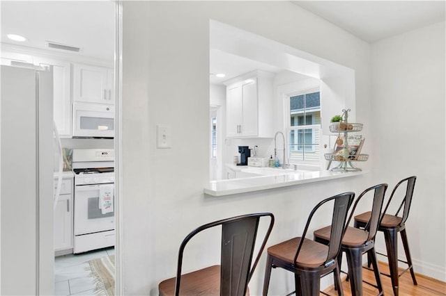 kitchen with white appliances, a breakfast bar area, sink, and white cabinets