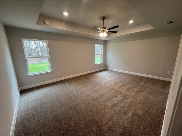 spare room featuring a tray ceiling, baseboards, visible vents, and dark carpet