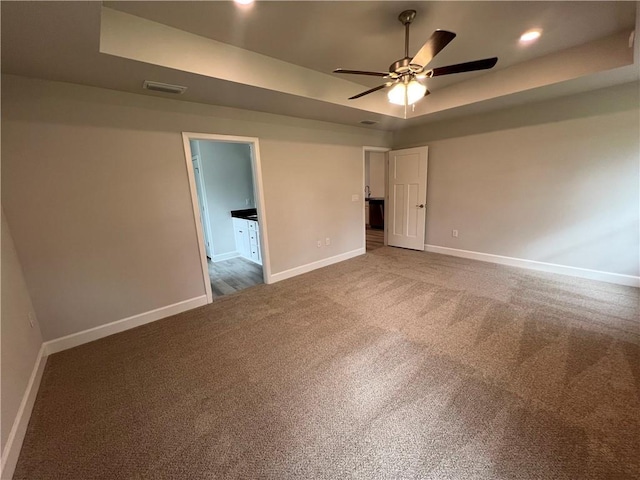 unfurnished bedroom with recessed lighting, a tray ceiling, baseboards, and carpet flooring