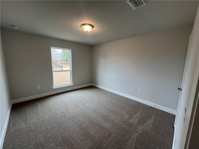 spare room featuring visible vents, dark colored carpet, and baseboards